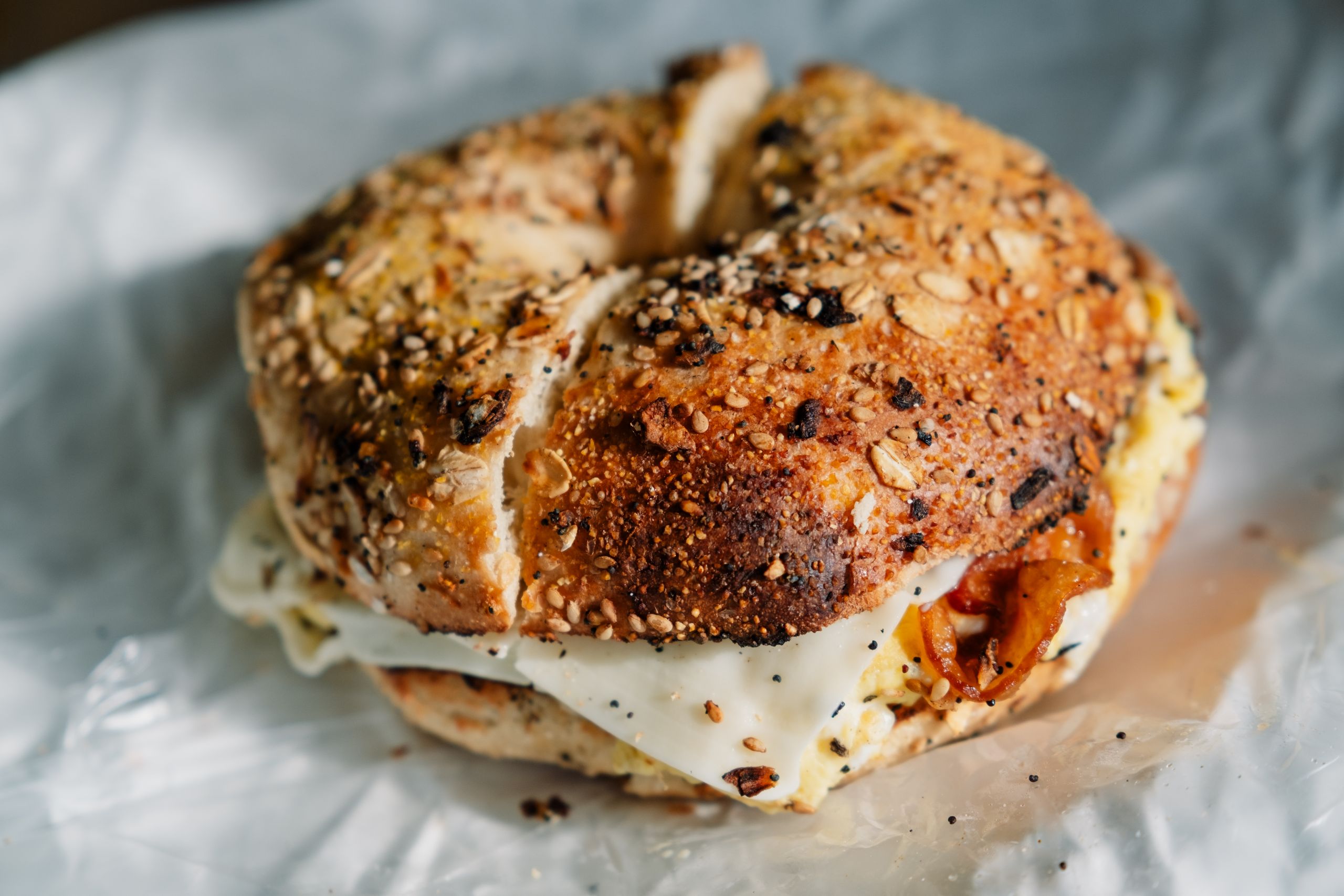 Close-up of a savory everything bagel sandwich stuffed with egg and bacon.