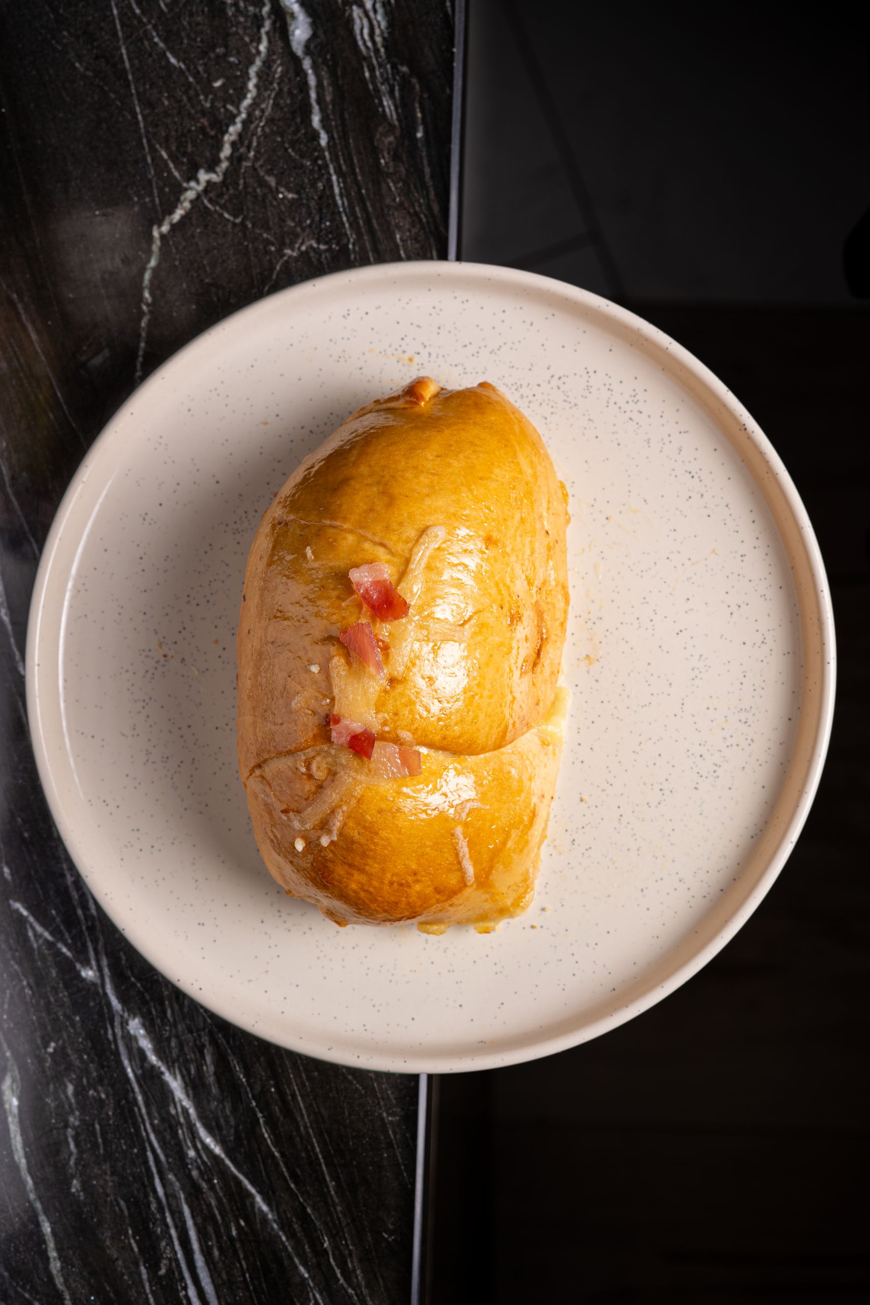 Top view of a freshly baked bread roll on a ceramic plate placed on a marble countertop.